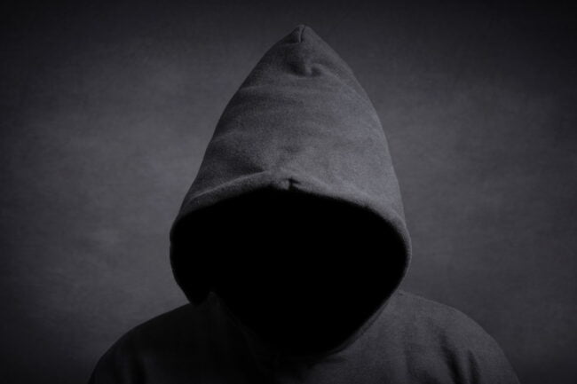 man in a hoodie with no face visible against dark background